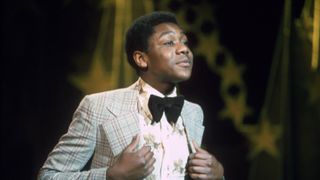 A young Lenny Henry in a check jacket and bow tie performs on New Faces in 1975.