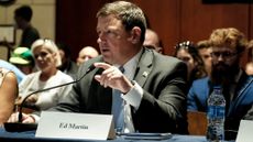 Ed Martin during a hearing connected to January 6 defendants. Martin is in a dark grey suit with a placard with his name in front of him as he points