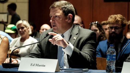 Ed Martin during a hearing connected to January 6 defendants. Martin is in a dark grey suit with a placard with his name in front of him as he points