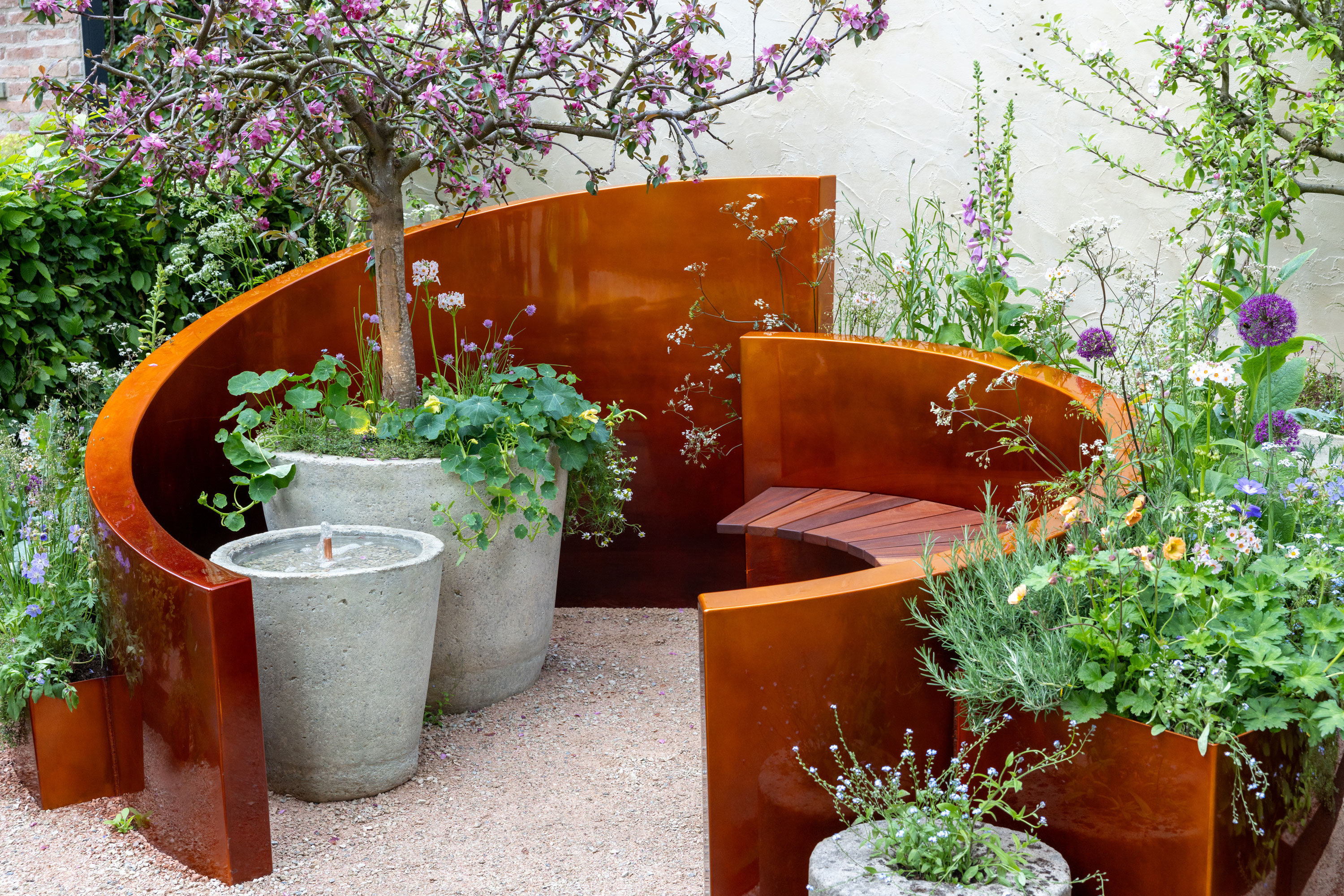 small seating area with containers, one planted with a small apple tree with blossom, and other plants such as nasturtium, allium and chives