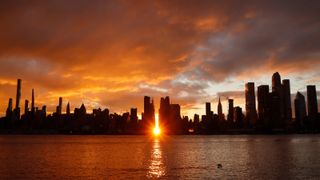 The sky turns orange as the sun rises above 42nd Street during a Manhattanhenge sunrise behind midtown Manhattan in New York City on November 28, 2022, as seen from Weehawken, New Jersey.