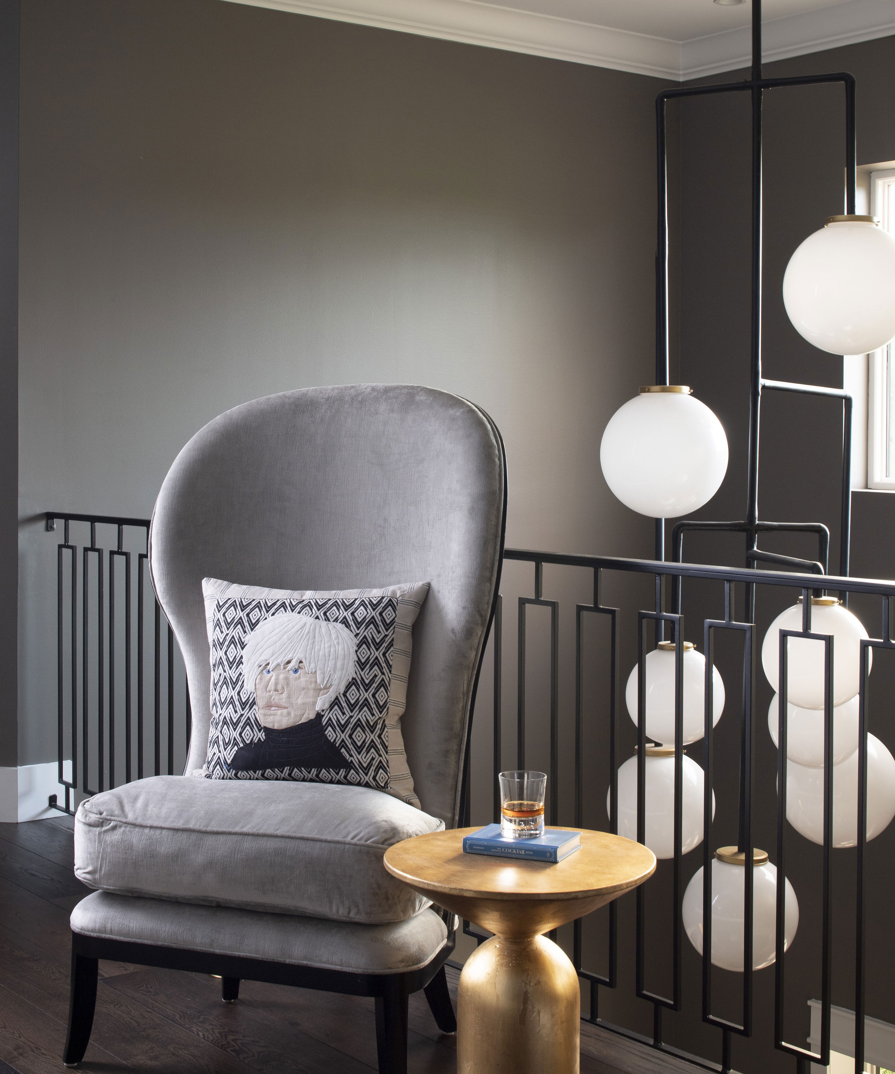 Living room paint ideas in earthy dark gray, with a gray armchair, gold side table and globe lights.