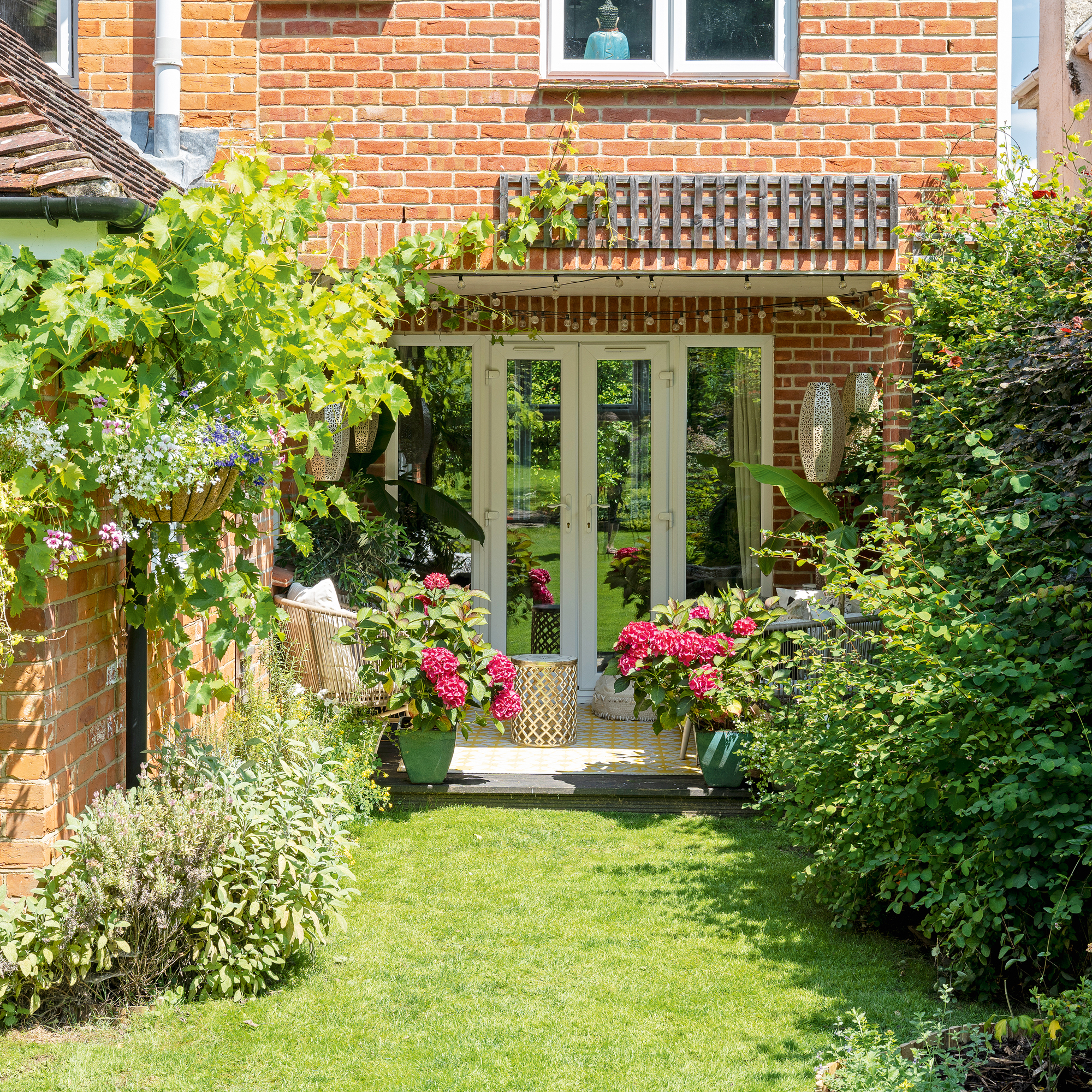 a garden with the view of a small patio area with a a pair of two seater outdoor sofas and potted hydrangeas