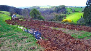 large field with countryside view and trenches being dug in ground with digger