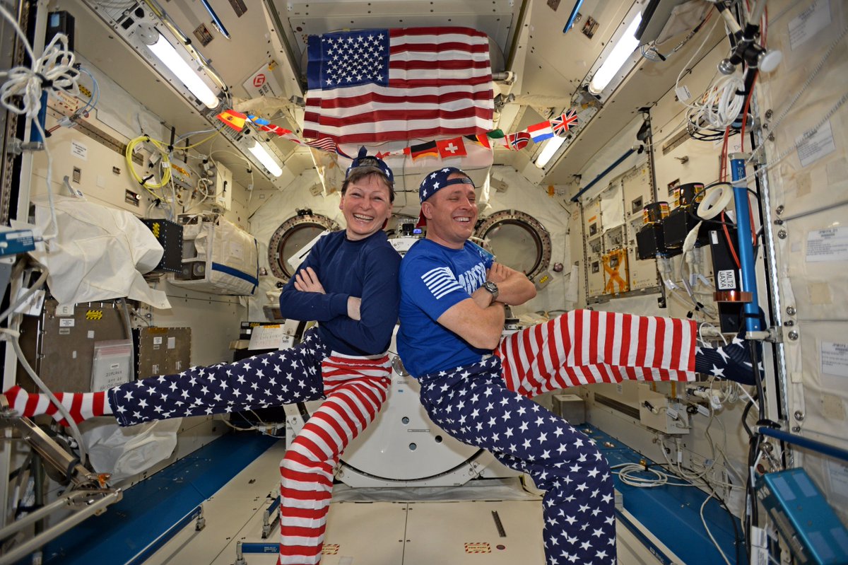 Two astronauts pose back to back in an ensemble of red, white and blue clothing