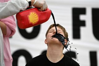 Activists from the climate change protest group Extinction Rebellion, pour a black liquid to represent oil, into the mouth of a fellow activist as they demonstrate against oil giant Shell on the beach in St Ives, Cornwall on June 11, 2021, on the first day of the three-day G7 summit being held from 11-13 June. -