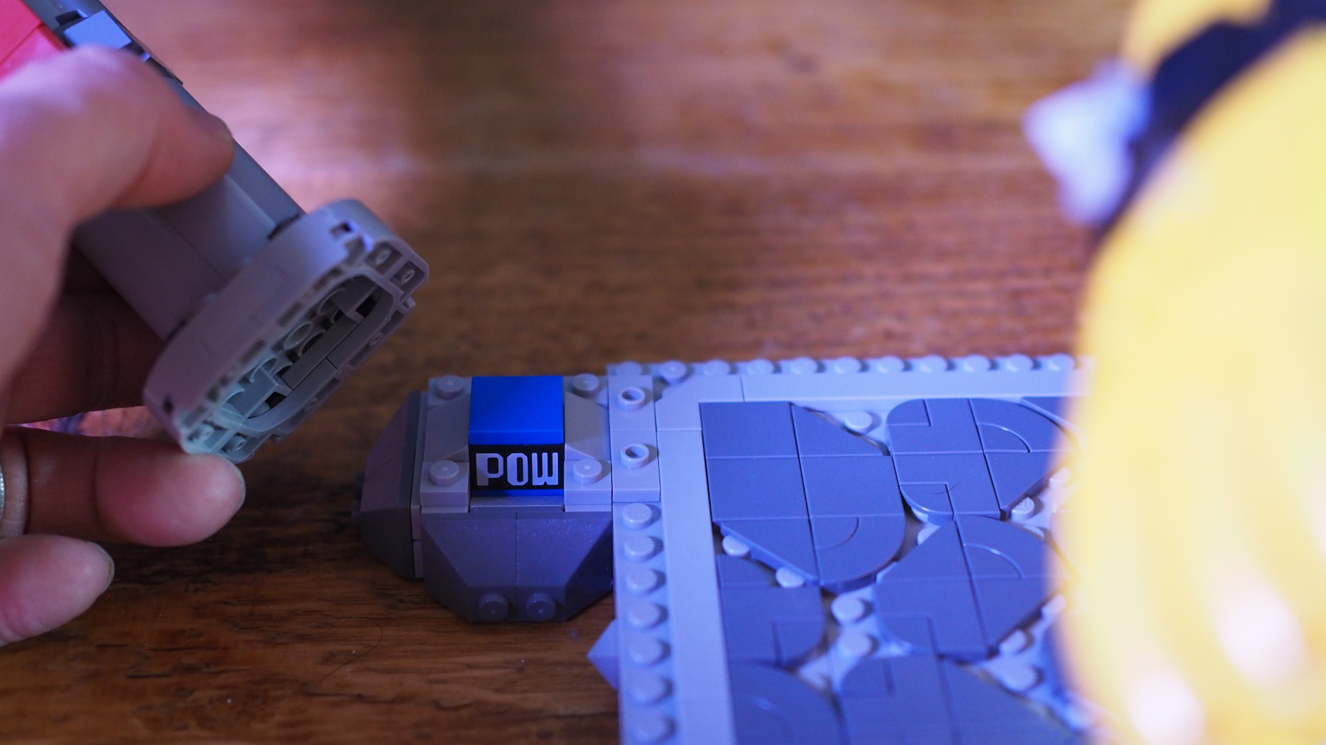 A hand lifts the torch off a 'pow' symbol on the base of the Lego The Mighty Bowser