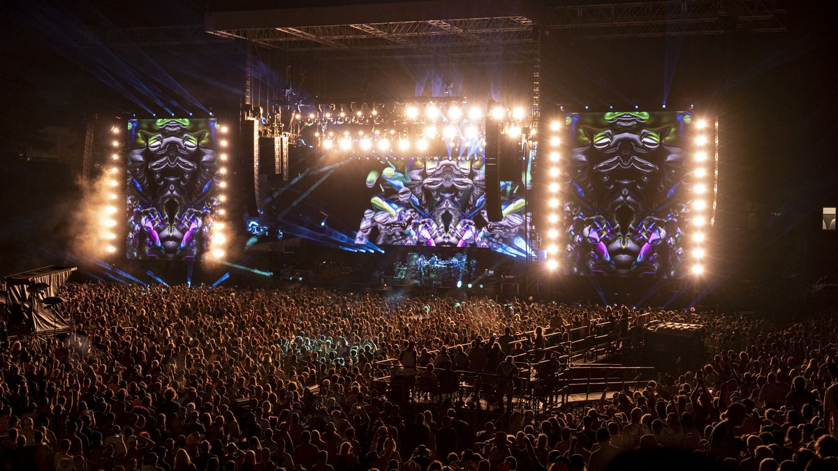 Dead &amp; Co perform at night on a stage with bright lights and colors as onlooking Deadheads dance.