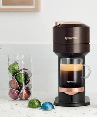 A mug on the Nespresso coffee maker on a white work surface surrounded by Nespresso pods.