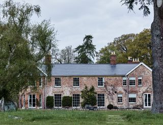 Exterior of brick Georgian home with bay and sash windows and mature trees