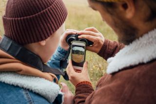 father and son holding binoculars in front of smartphone