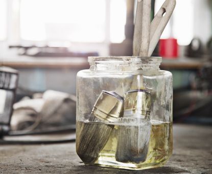 A glass jar filled with water with two dirty paintbrushes inside