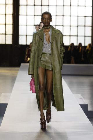 Gucci model wearing a green leather coat with a gray shirt and matching green leather short shorts.