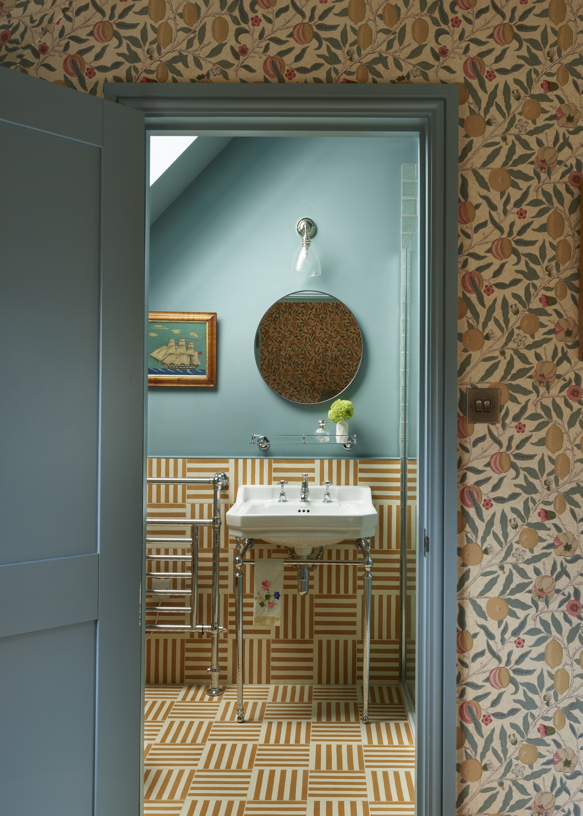 an ensuite bathroom with teal colored walls, striped ochre tiles and a washbasin on legs. Shown with similar hues in the adjoining bedroom
