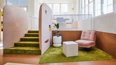 Living area with pink lounge chair, white tiled side table, green carpet and cork flooring and walls