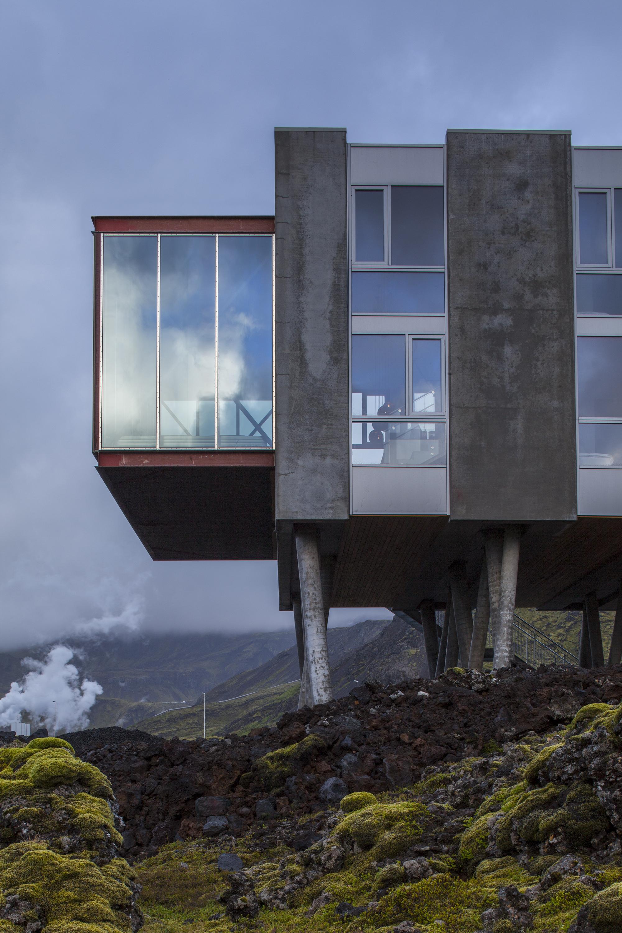 A hotel is nestled atop rocky formations in an Icelandic desert landscape, with floor-to-ceiling windows and minimal furnishings letting the outdoors in.