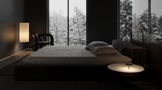 Image of a luxury black bedroom with a giant bed in the middle. There are two lamps on in the room and there is snow outside the window.