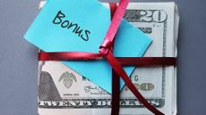 Cash wrapped up with a red gift ribbon and a sticky note on top that reads "bonus" 