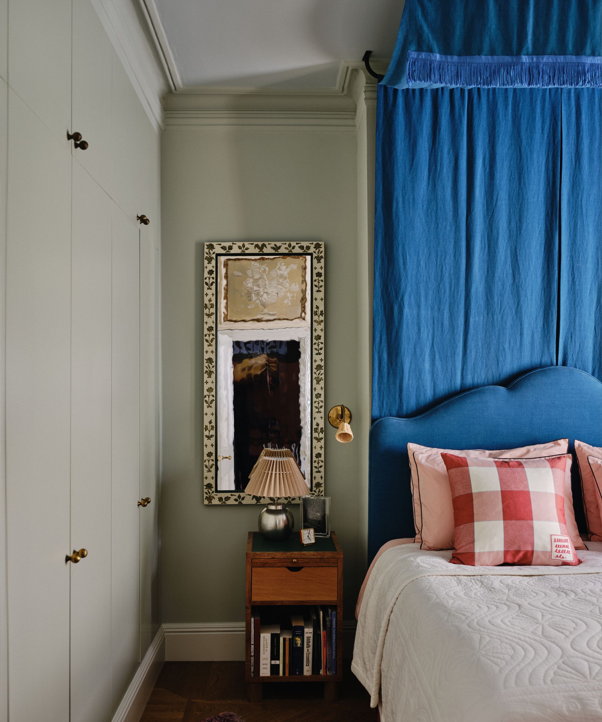 A bedroom with gray-green walls, light gray-green ceiling, a bed with a bright blue headboard, and a matching canopy.