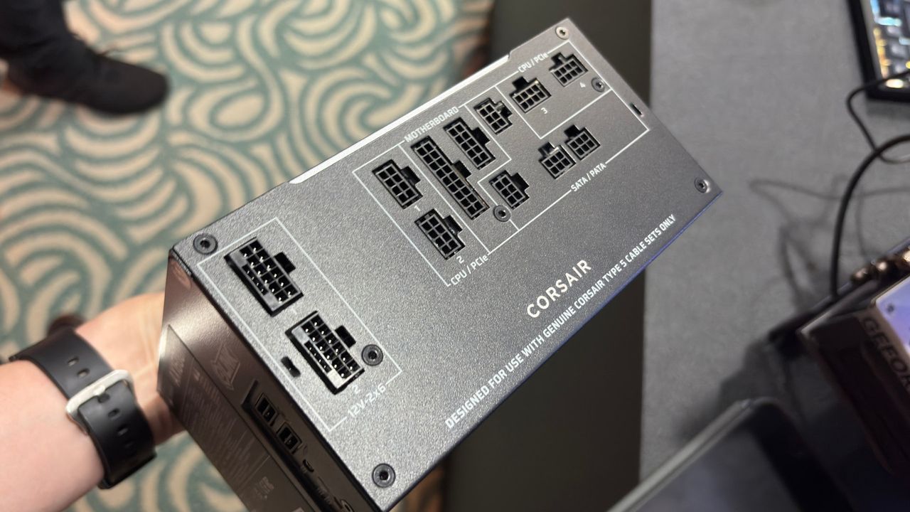 A photo of a Corsair AX1600i Shift PSU being held in a hand, showing the unit's power connectors