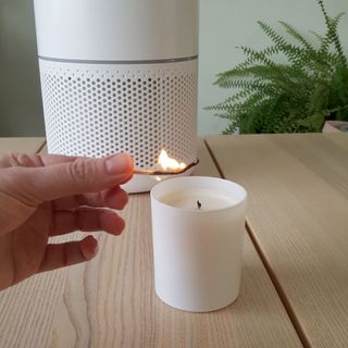 A lit match and a candle in front of a white air purifier