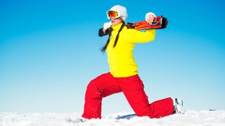 Woman doing lunges at ski resort holding skis