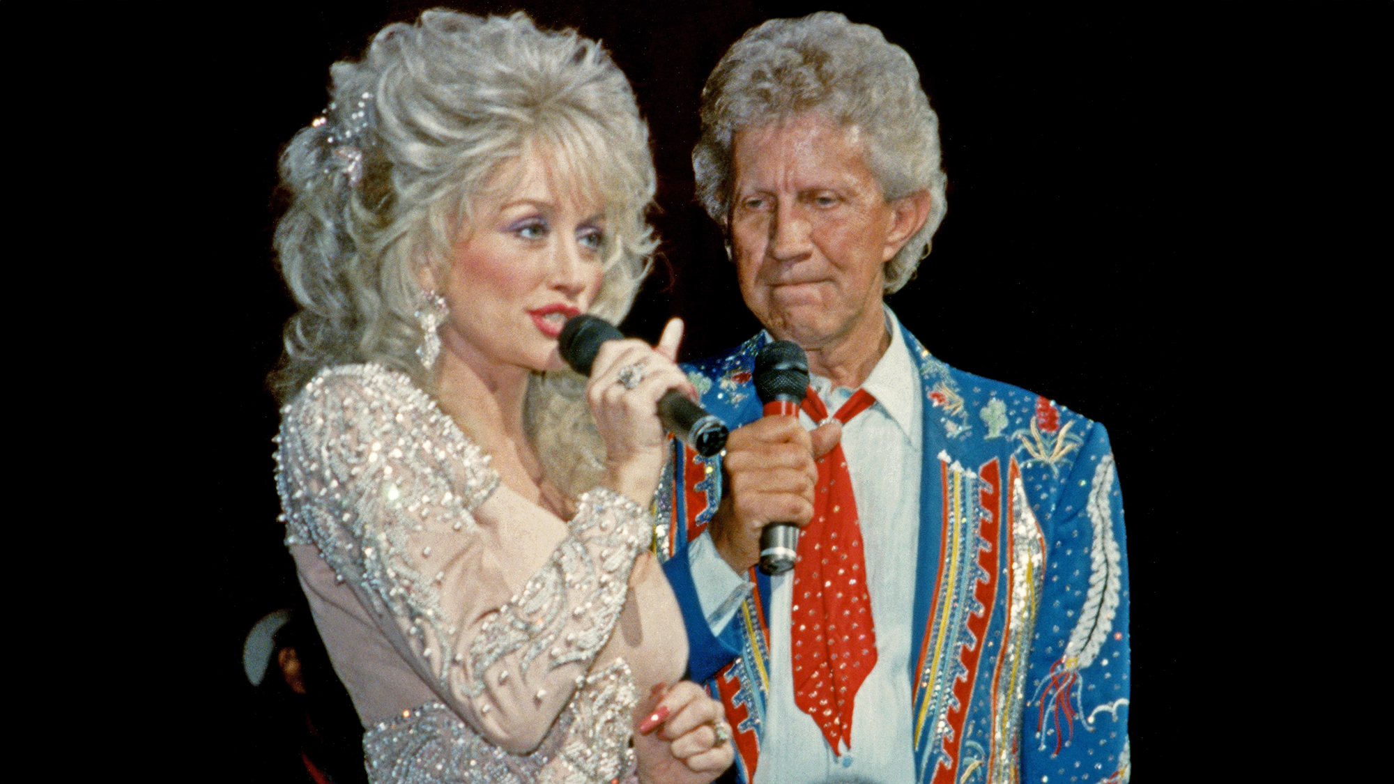Former duet partners, American singer-songwriter, actress, and businesswoman Dolly Parton and American country music singer Porter Wagoner (1927-2007), sing on stage circa 1990's at the Grand Ole Opry in Nashville, Tennessee.