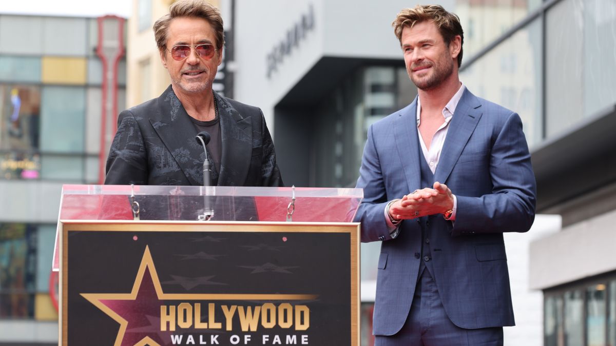 Robert Downey Jr. speaking at a podium while Chris Hemsworth happily watches on, during his Hollywood Walk of Fame ceremony.