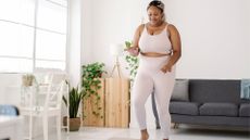 woman wearing a light pink leggings and crop top set doing some standing walking exercise in a living room setting. 