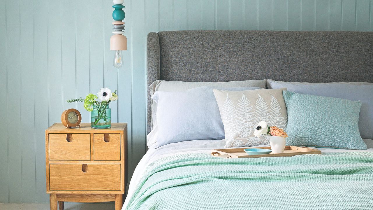 A bedroom with a fabric headboard on the bed, a vintage bedside table and a statement pendant light