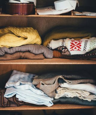 a close up photo of wooden closet shelves with stacks of clothing items on them