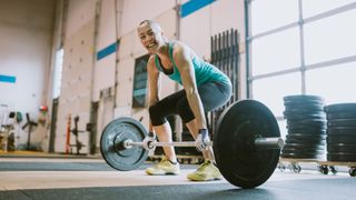 Woman bending over to do a deadlift with a barbell as part of the 5x5 workout