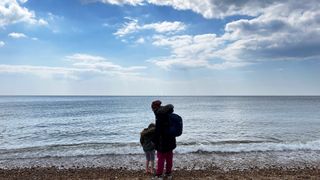 Mother and son stood on edge of beach looking at sea and clouds