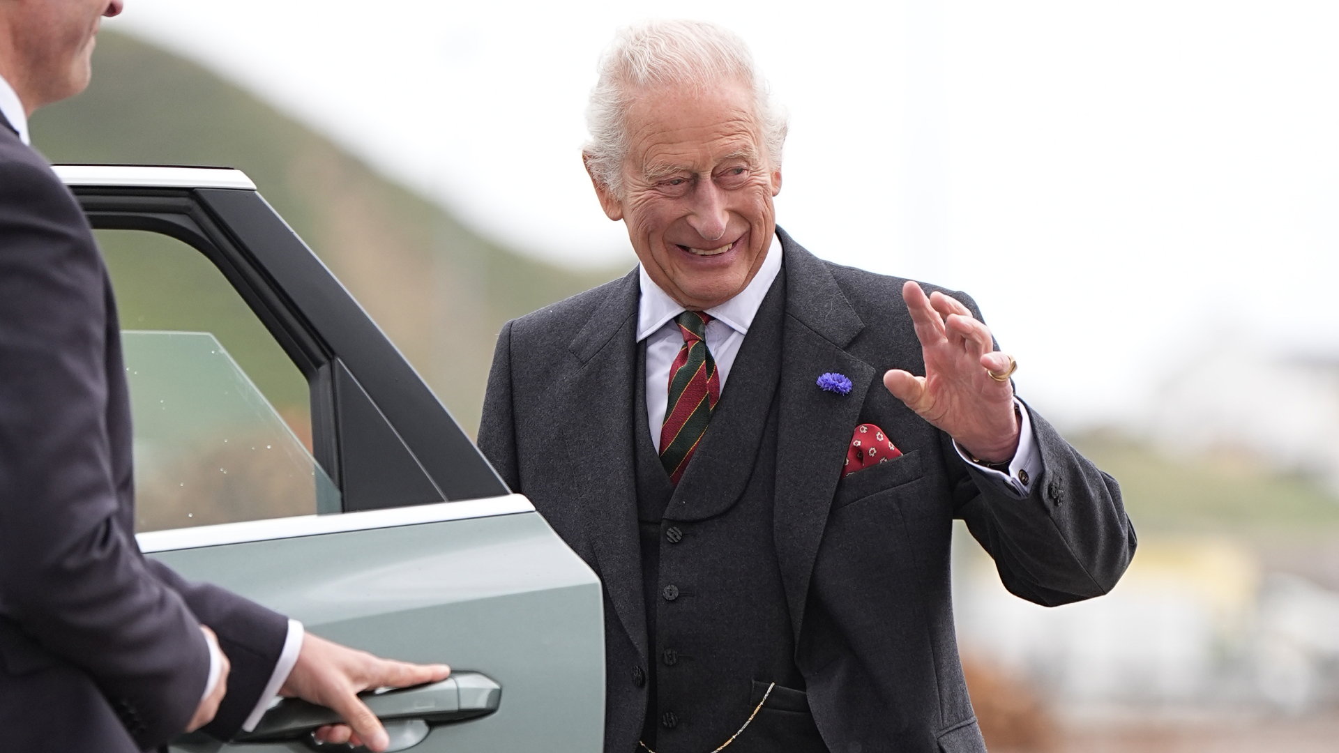 King Charles waving and smiling while getting into a car