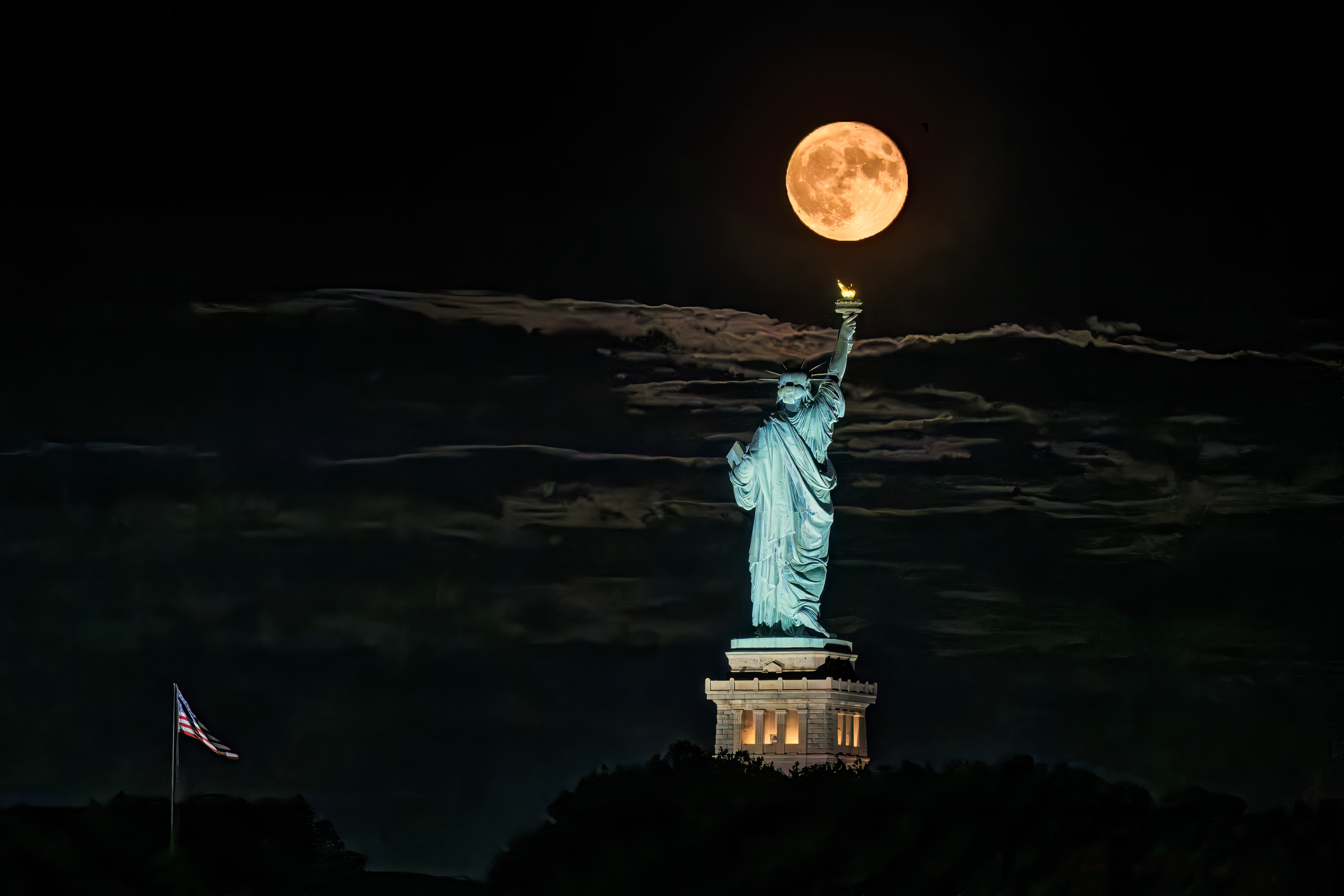 A full moon hangs over the statue of liberty