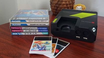 Hyperkin Retron GX next to stacked PC Engine game cases and Hucards in front.