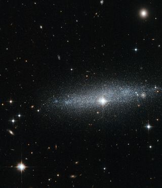 A wide view of the dwarf Glitter Galaxy with bright stars all around.