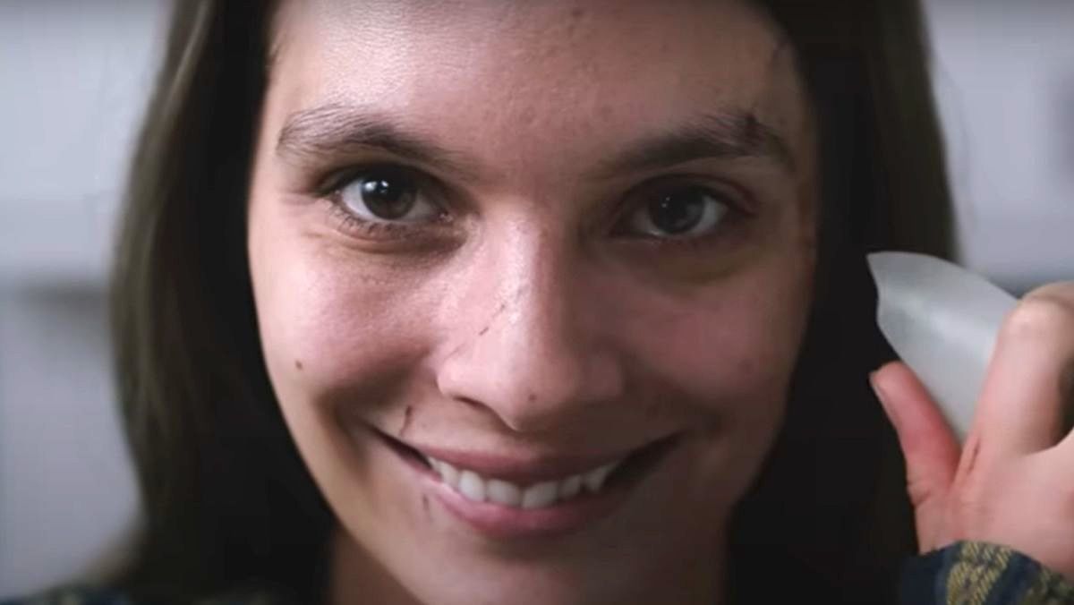 Smile star Caitlyn Stasey as a patient smiling and holding a shard of vase up to her face.