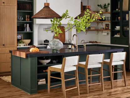 A kitchen with cabinetry and island painted in a deep forest green shade with boucle bar stools and wooden floors