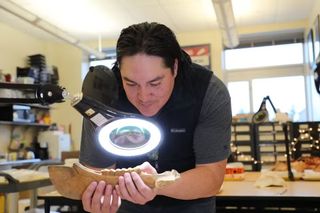 A man holds a horse bone and examines it under a light in a laboratory