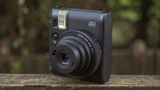 An Instax Mini 99 camera, on a wooden surface in a woodland setting