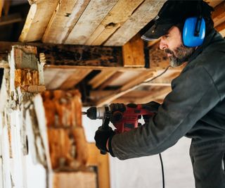 man wearing heard hat and googles drilling timbers