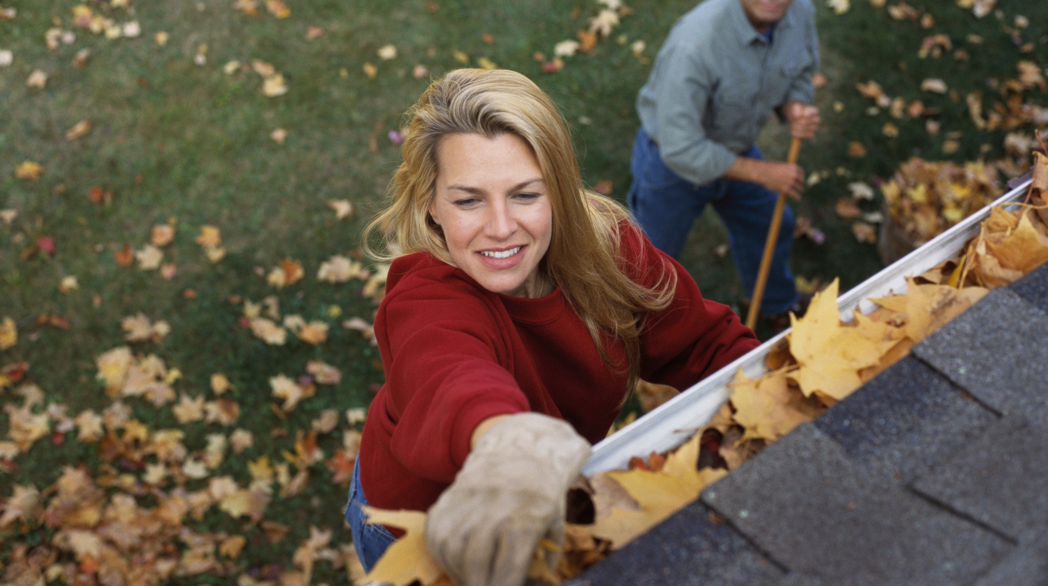 A couple cleaning the gutters of their home