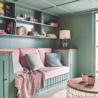 Green living room with built-in sofa with pink cushions.