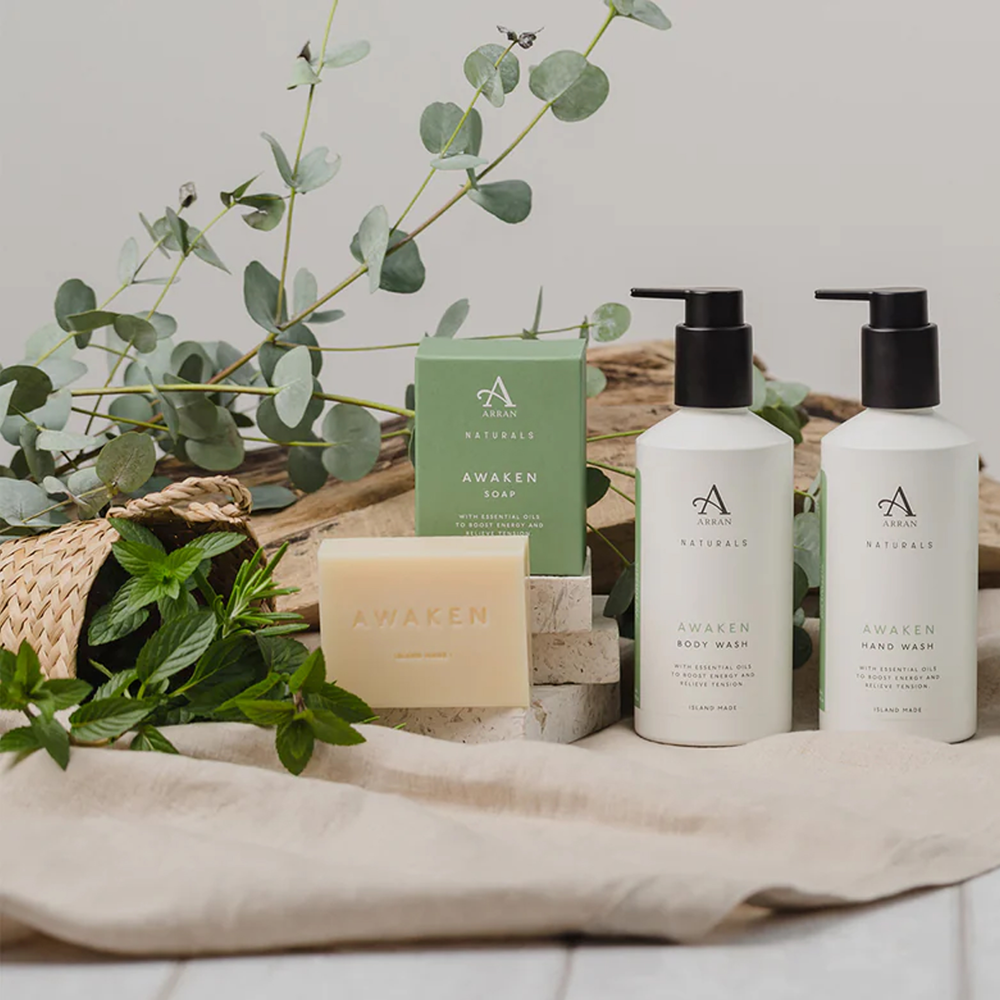 Two bottles of Arran Awaken shower gel and a bar of soap next to a bunch of mint and eucalyptus