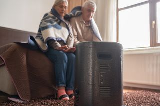 Two elderly people sitting with a blanket by a heater