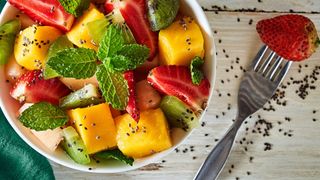 Fruit salad in a bowl with mango, strawberries, mint