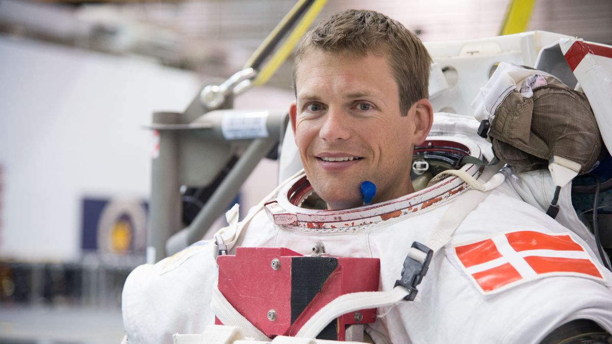 andreas mogensen visible in a spacesuit from the shoulders up, inside a large facility