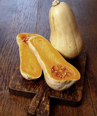 A butternut squash whole and sliced on a wooden board