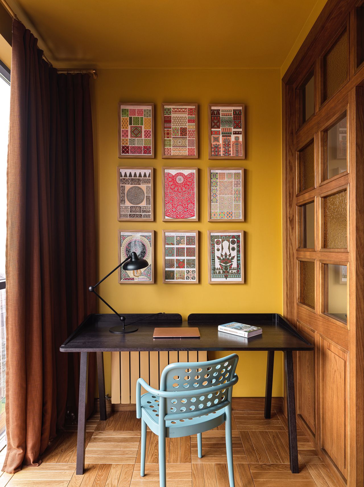 A home office situated next to the window, painted yellow, with dark toned furniture